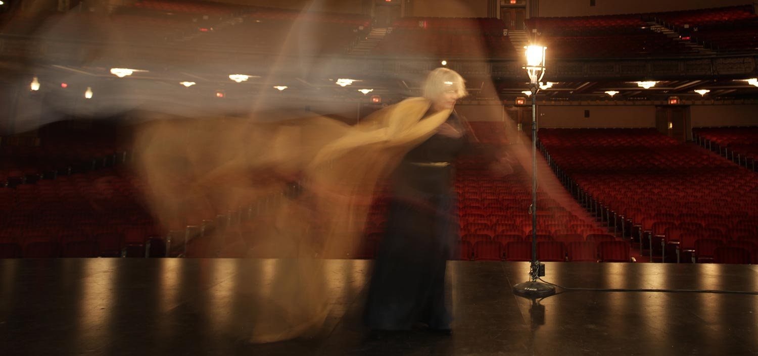 Betty Buckley on an empty stage beside the ghost light, a gold scarf in motion
